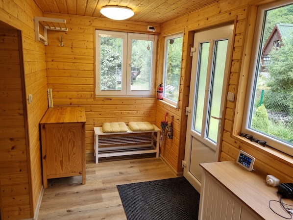 Interior de una cabaña de madera con un banco, una mesa pequeña y una ventana con vista a la vegetación.