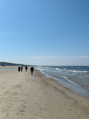 A beach with people walking along the shore, waves crashing onto the sand, and a clear sky. - Summer house with two terraces near Rødhus Strand (Pandrup)