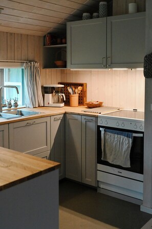 A kitchen with a stove, oven, sink, and a coffee maker. - Summer house with two terraces near Rødhus Strand (Pandrup)