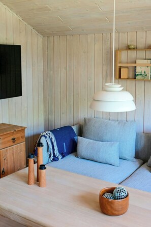 A room with a wooden wall, a sofa with blue cushions, a wooden chest of drawers, and a hanging light fixture. - Summer house with two terraces near Rødhus Strand (Pandrup)