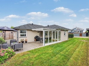 Ein Wohnhaus mit überdachter Terrasse, Sitzgelegenheiten im Freien und einem gepflegten Rasen.