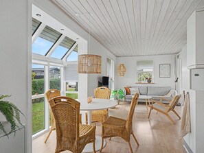 Ein geräumiger Raum mit einem großen Esstisch, umgeben von Korbstühlen, einer Couch und einem Fernseher.