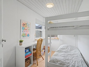 Ein Kinderzimmer mit Etagenbetten, einem Schreibtisch, einem Stuhl und einem Fenster.