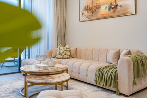 A living room with a sofa, a round coffee table, and a painting on the wall. - Sky Level 1BR with Balcony Overlooking the Canal, Short Drive from Burj Khalifa (Dubai)