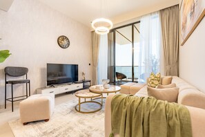 A modern living room with a flat-screen TV, a sofa, a coffee table, and a large window with curtains. - Sky Level 1BR with Balcony Overlooking the Canal, Short Drive from Burj Khalifa (Dubai)