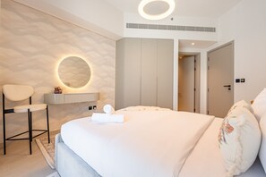 Een moderne hotelkamer met een groot bed, een ronde spiegel, een stoel en een badkamer die door een open deur zichtbaar is.