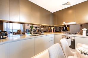 A modern kitchen with a central island, built-in appliances, and a dining area with a view. - Sky Level 1BR with Balcony Overlooking the Canal, Short Drive from Burj Khalifa (Dubai)
