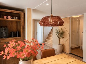 Una cuina moderna amb una cafetera, una taula de dinar amb un ram de flors i una escala que porta a una zona de dutxa.