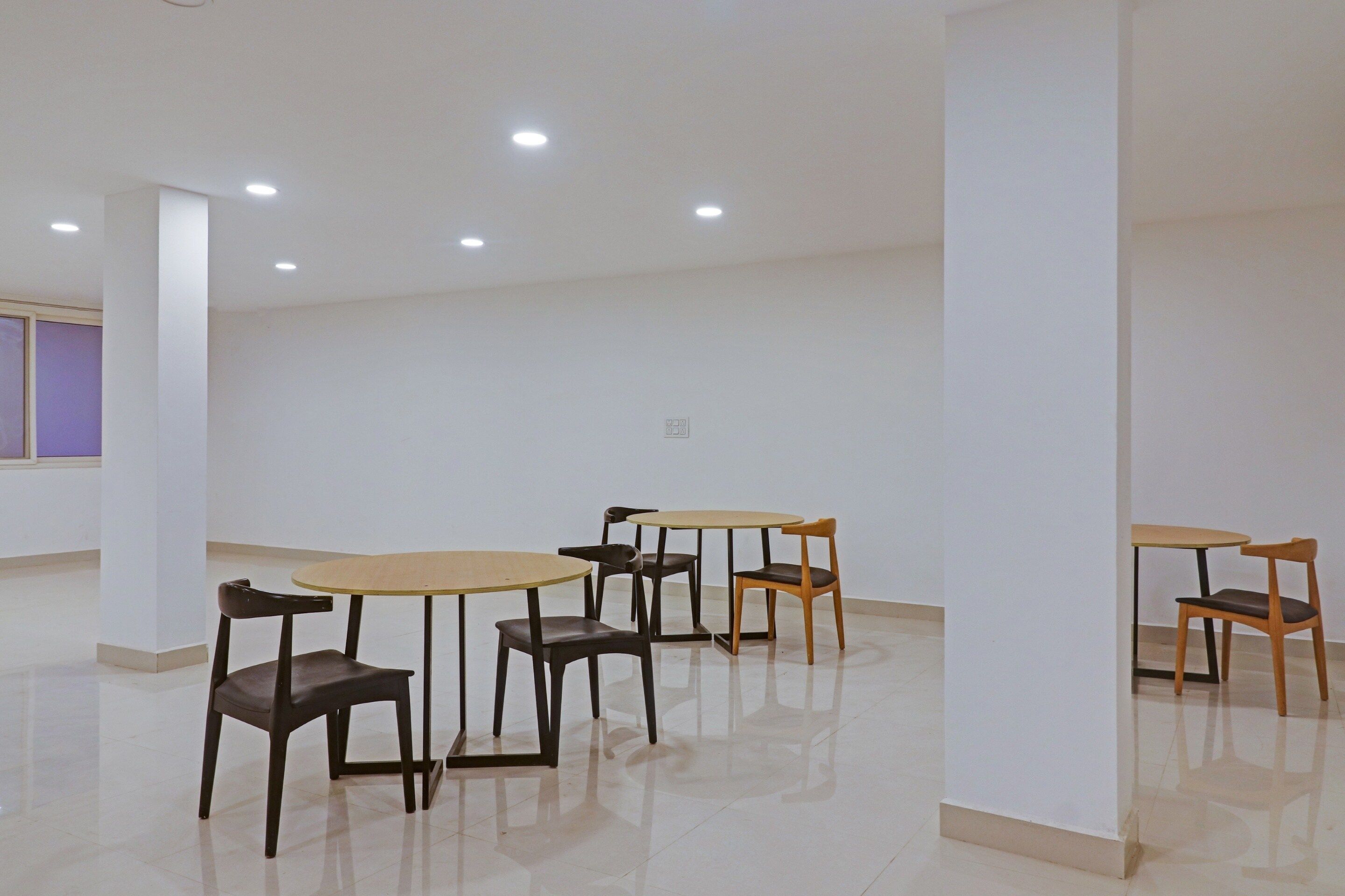 A room with white walls, a tiled floor, and several tables and chairs arranged for seating.
