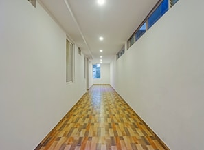 A hallway with a checkered wooden floor, white walls, and a window on the right.