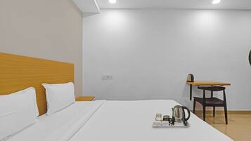 Habitación de hotel con cama, cabecero de madera, mesita con tetera y tazas, y una silla.