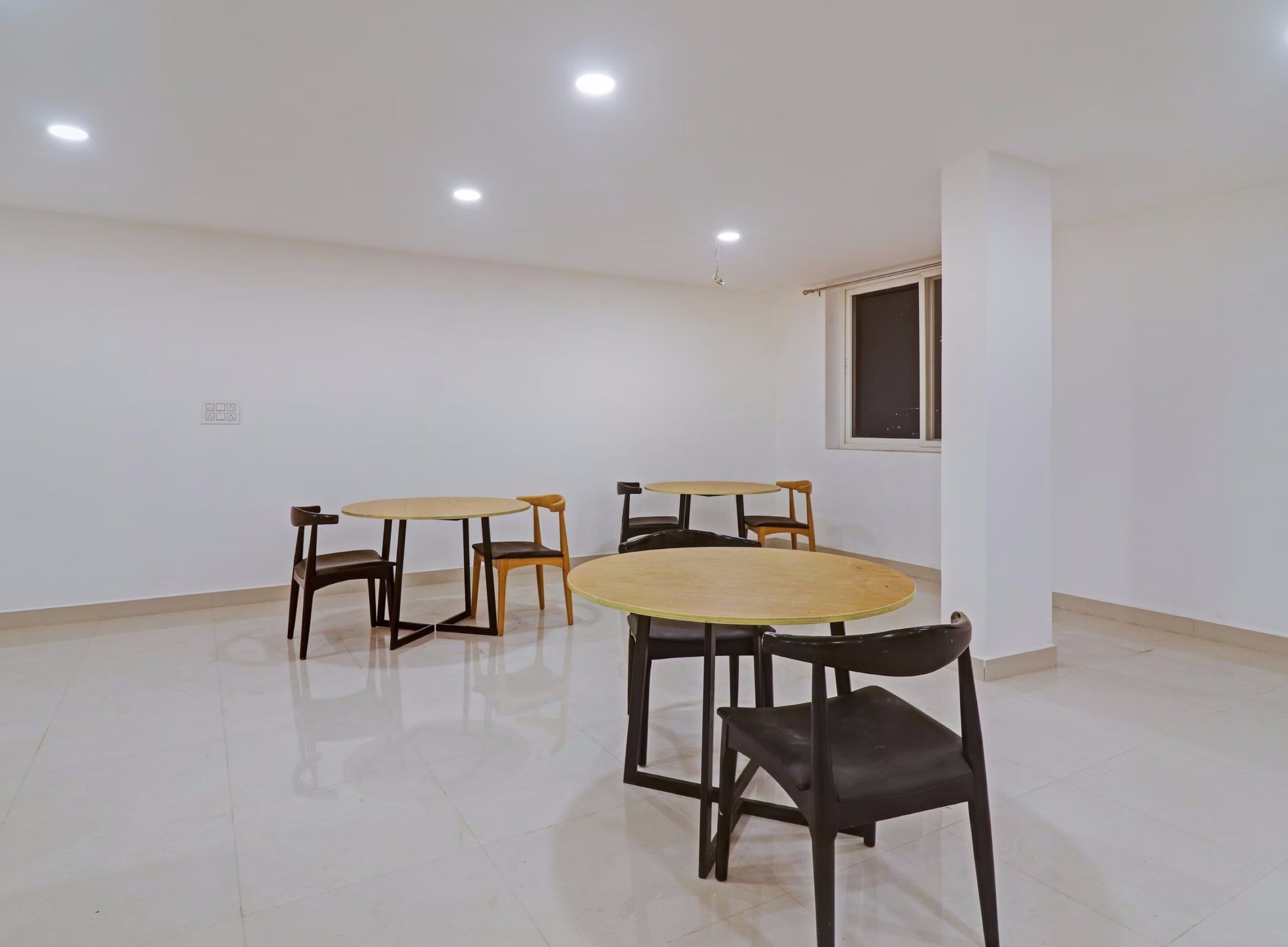 A room with four tables and chairs, a window, and recessed ceiling lights.