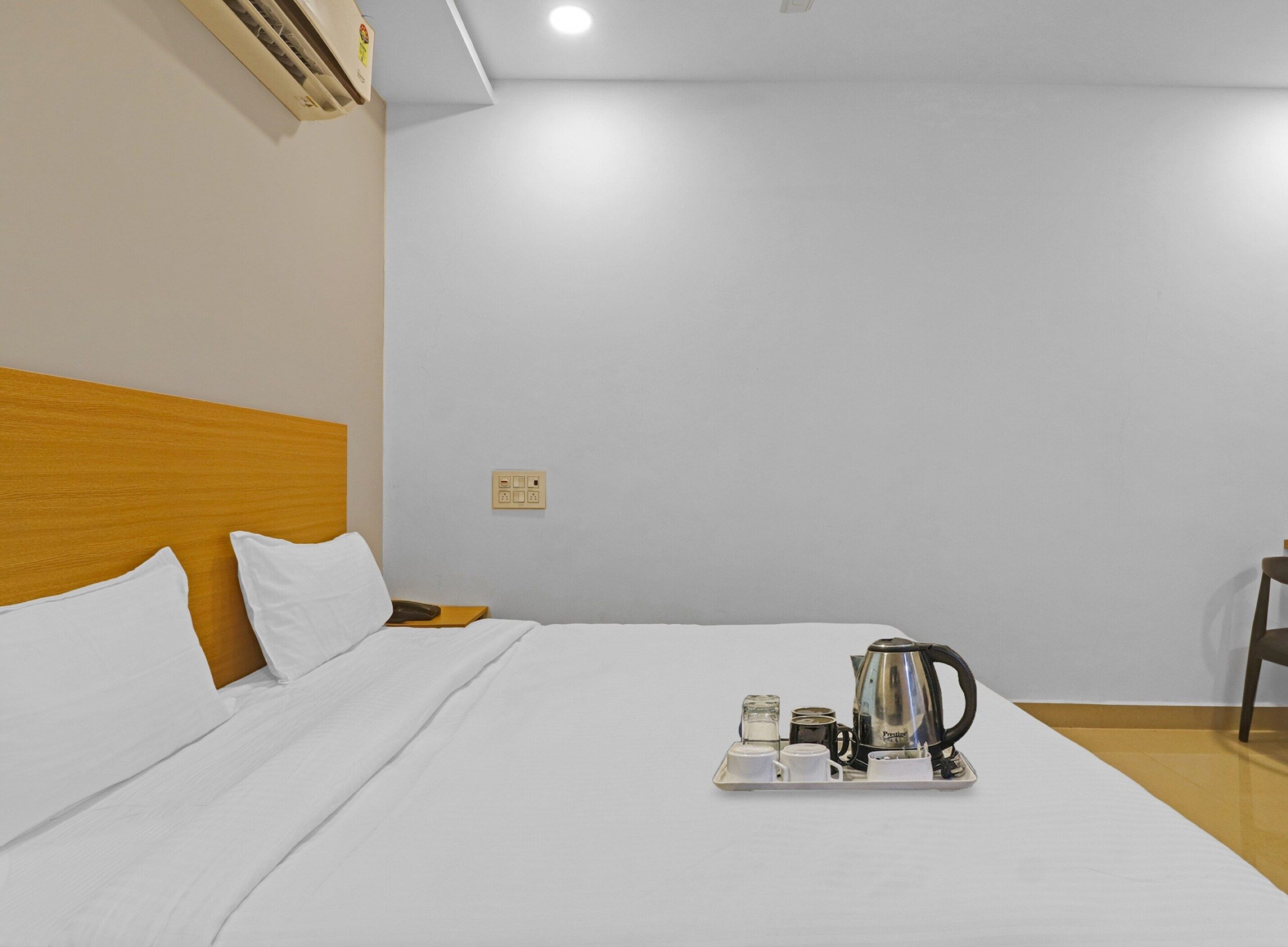 Habitación de hotel con una cama, una mesita de noche, una bandeja con cafetera, tazas y un hervidor.