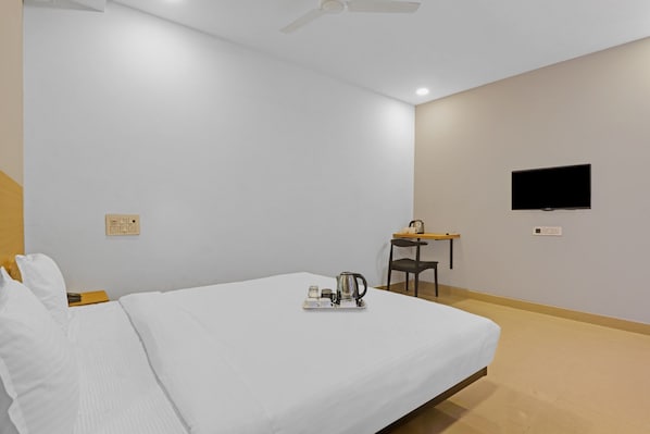 A hotel room with a bed, a desk, a chair, a television, and a tray with a kettle and cups.