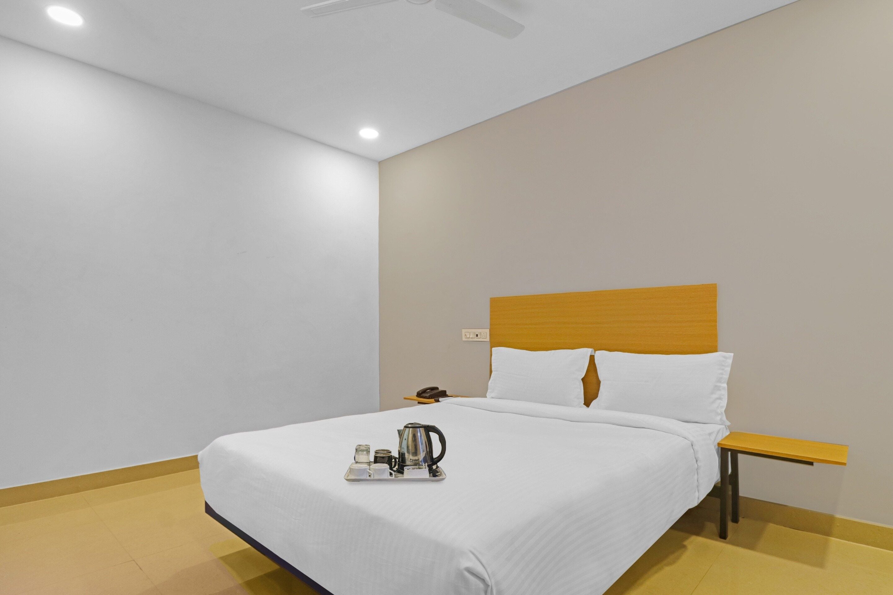 A hotel room with a bed, a bedside table with a phone, and a tray with a kettle and cups.