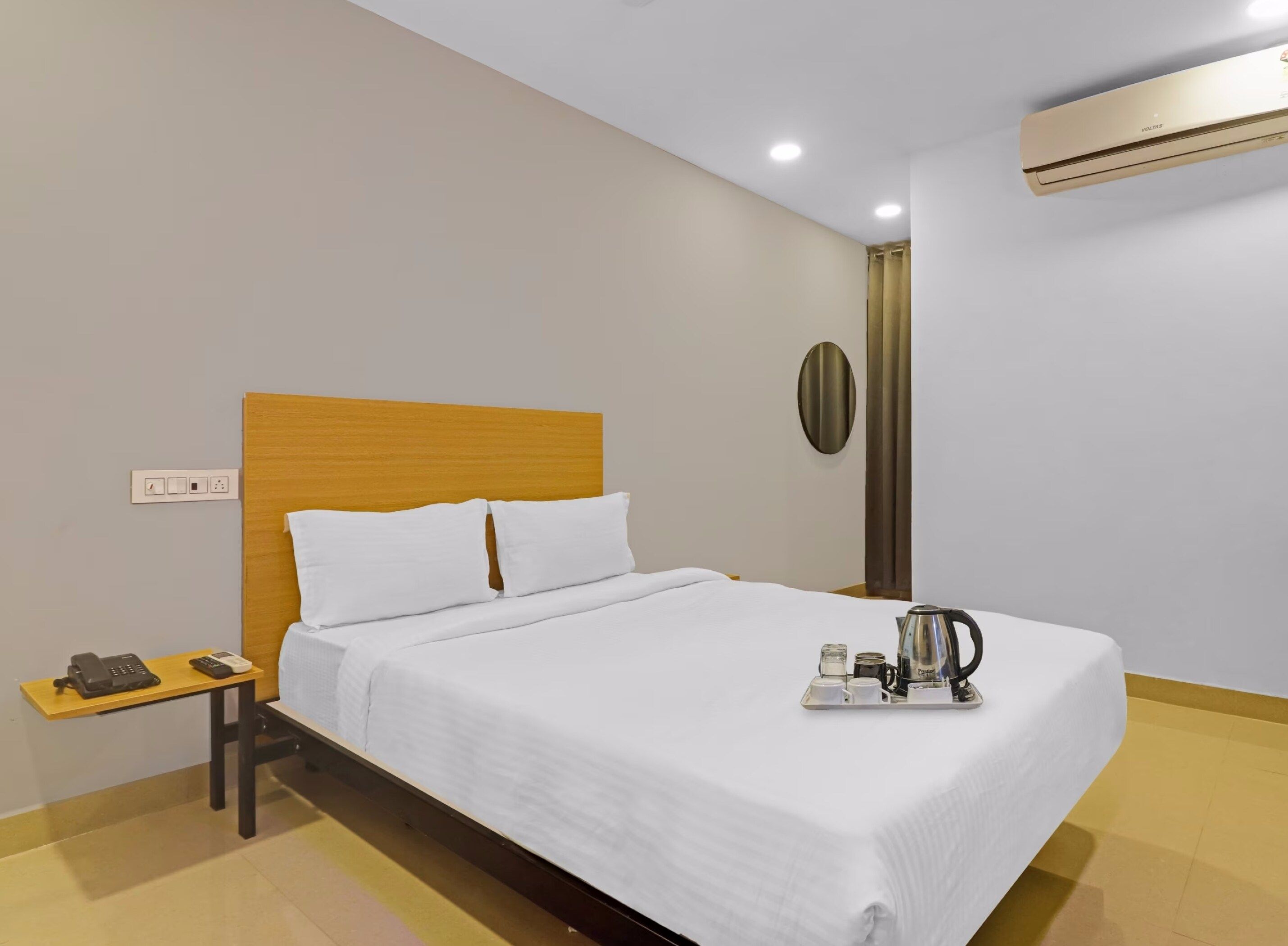 A hotel room with a bed, bedside table, and a tray with a kettle and cups.