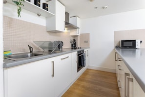 A modern kitchen with white cabinetry, a stainless steel sink, a microwave, and a built-in oven. - Flatzy - Prime City Apartment 2 Baths Sleeps 6 (Merseyside)