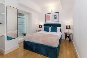 A modern bedroom with a bed, bedside lamps, a window with blinds, and a mirror. - Flatzy - Prime City Apartment 2 Baths Sleeps 6 (Merseyside)