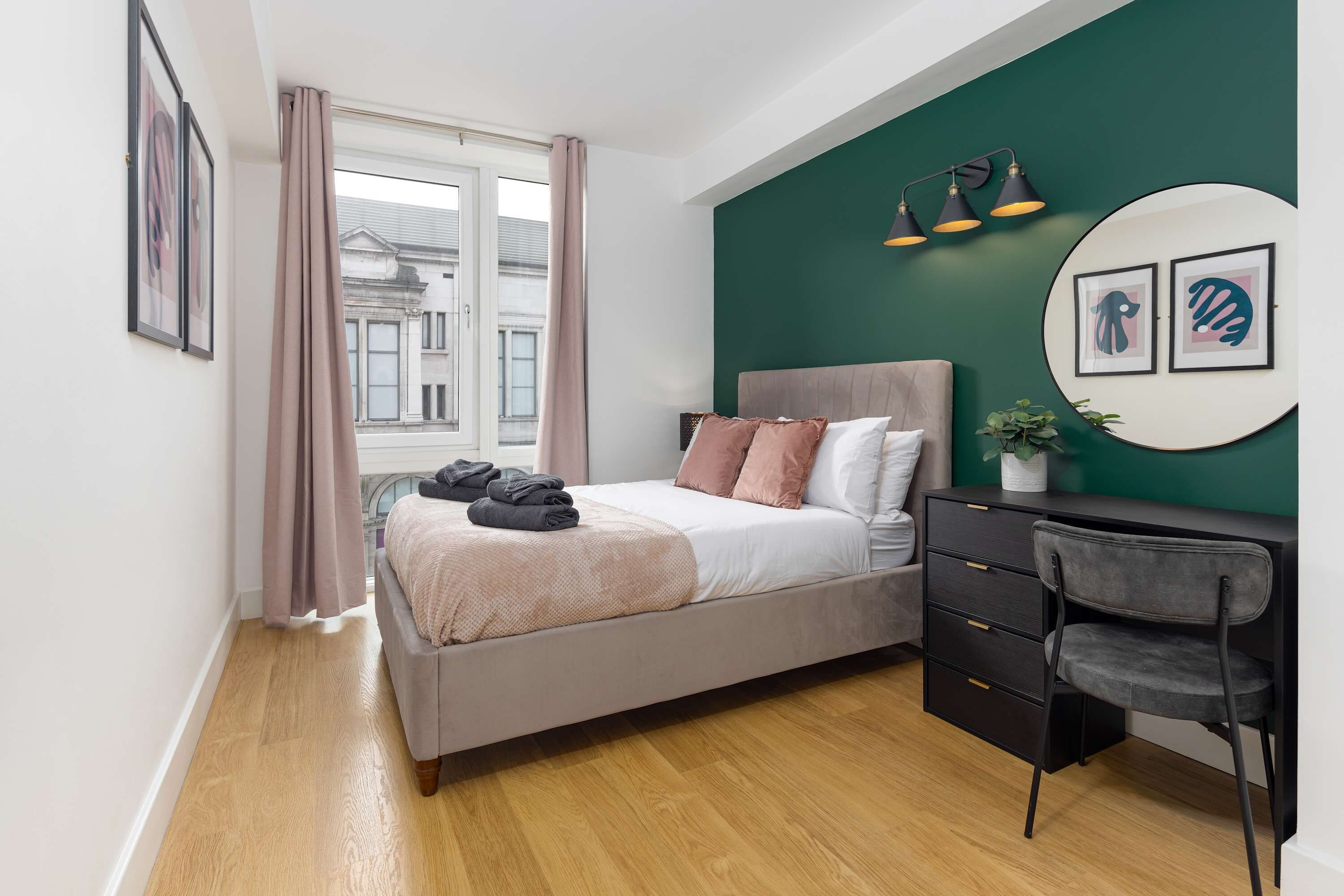 A bedroom with a bed, a desk, a chair, a potted plant, and artwork on the walls.