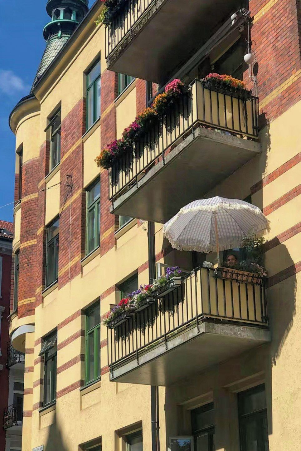 Un immeuble à plusieurs étages, doté de balcons ornés de jardinières et surmonté d’un parasol blanc.