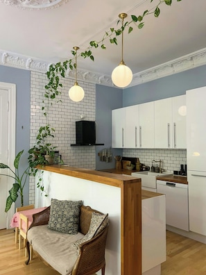 A modern kitchen with white cabinets, a brick backsplash, and hanging plants. - Moody vintage apartment in Oslo (Oslo)