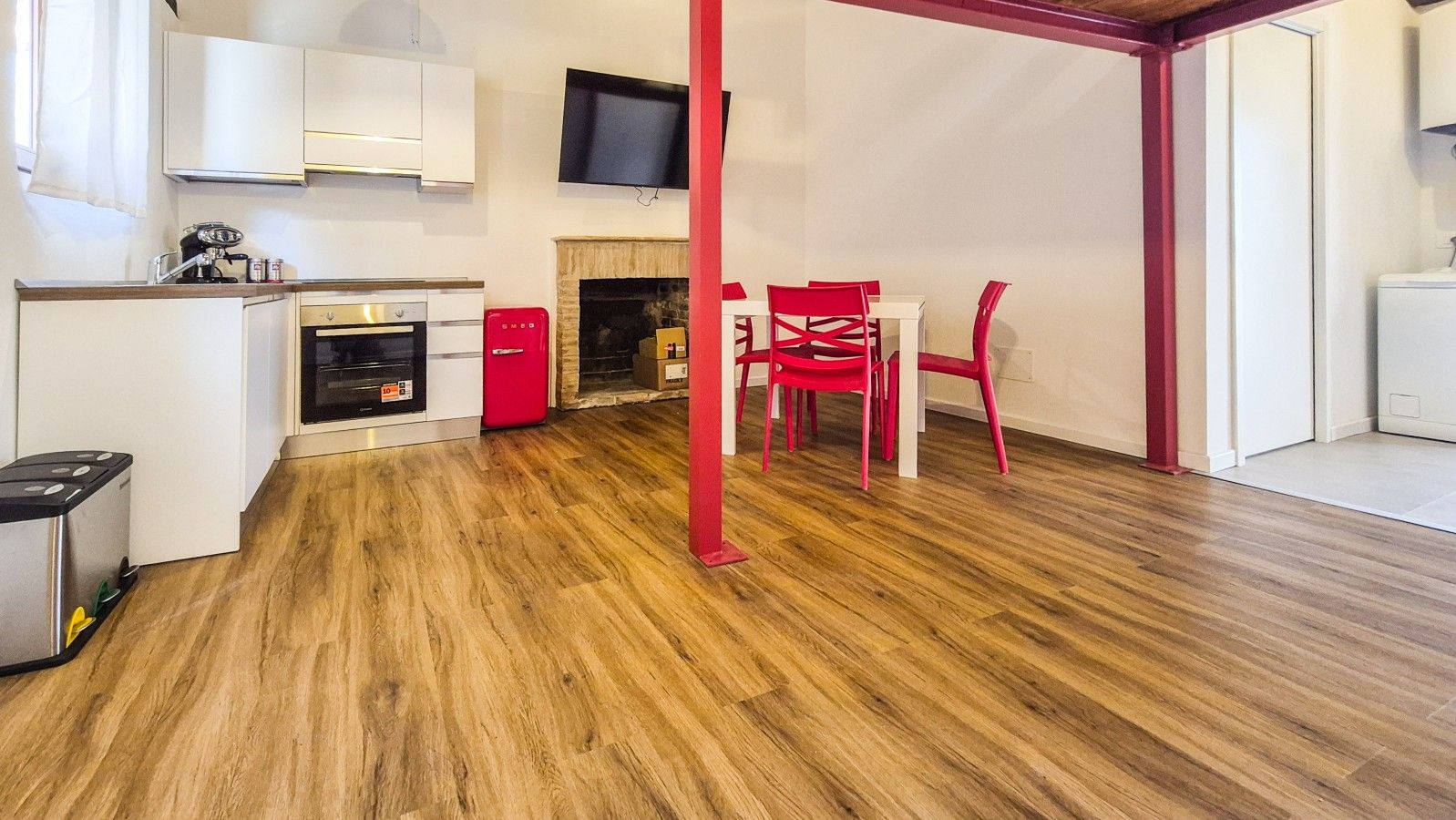 A modern kitchen with white cabinets, a red refrigerator, and a built-in oven.