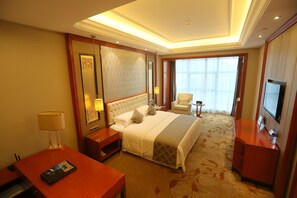 A hotel room with a large bed, a desk, a chair, a TV, and a window with curtains.