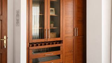 A bedroom with a large wooden wardrobe, a bed with a white quilt, and a small window with curtains.