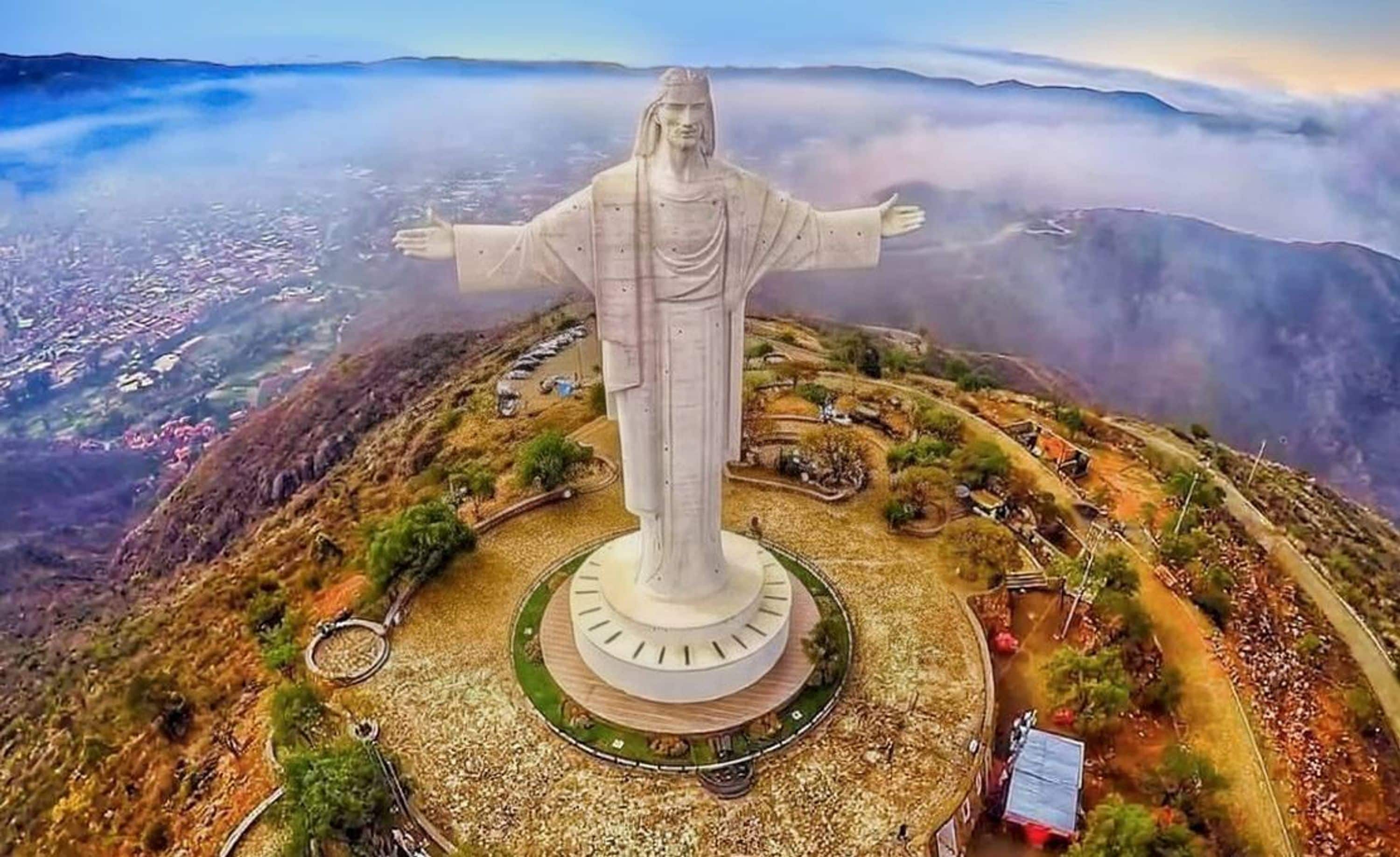 Una estatua grande con los brazos extendidos, rodeada por una plataforma circular y un área ajardinada con senderos y edificios pequeños.