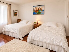 Quarto de hotel com duas camas, um quadro, um abajur e uma janela com cortinas.