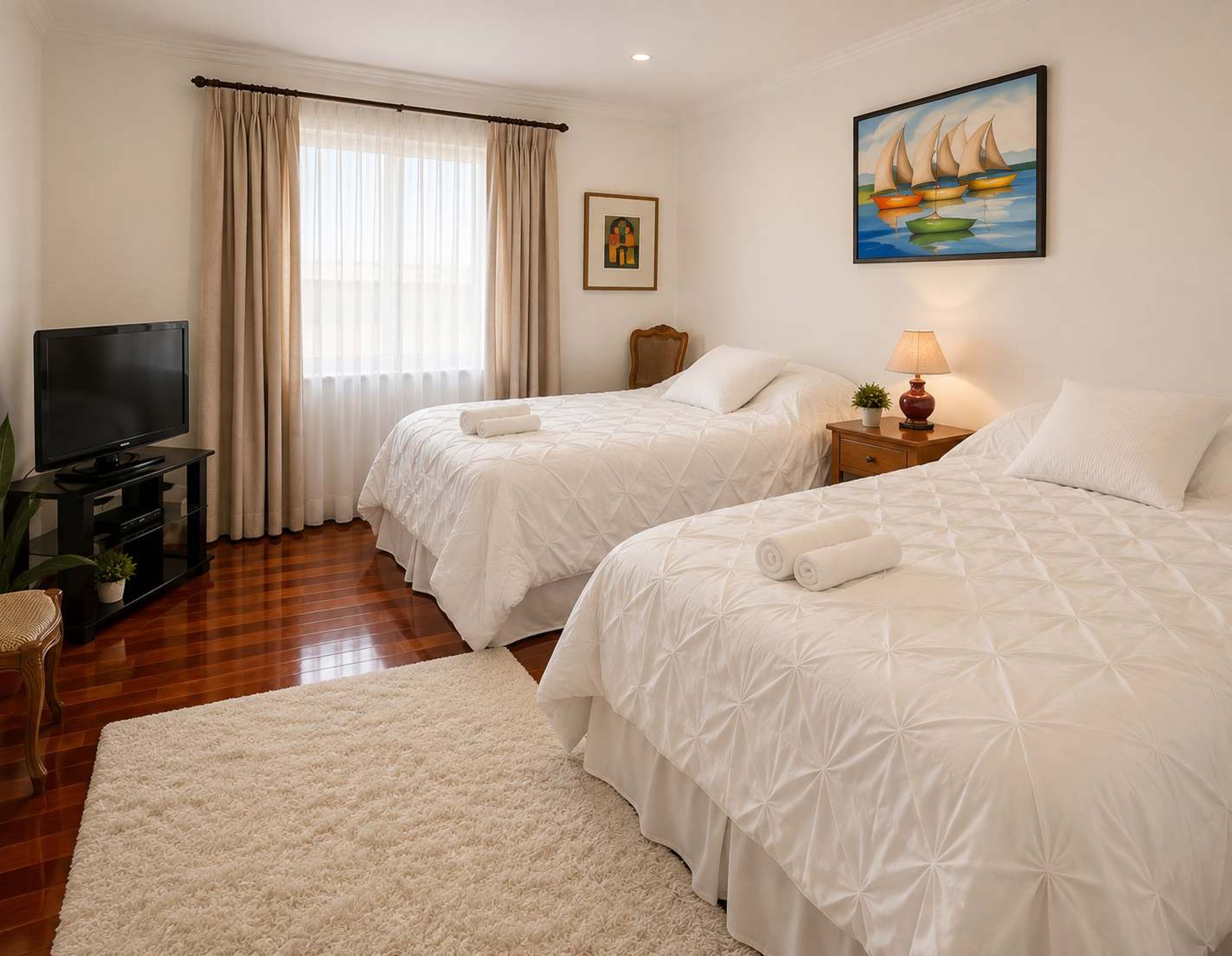 A hotel room with two beds, a television, a painting, and a window with curtains.