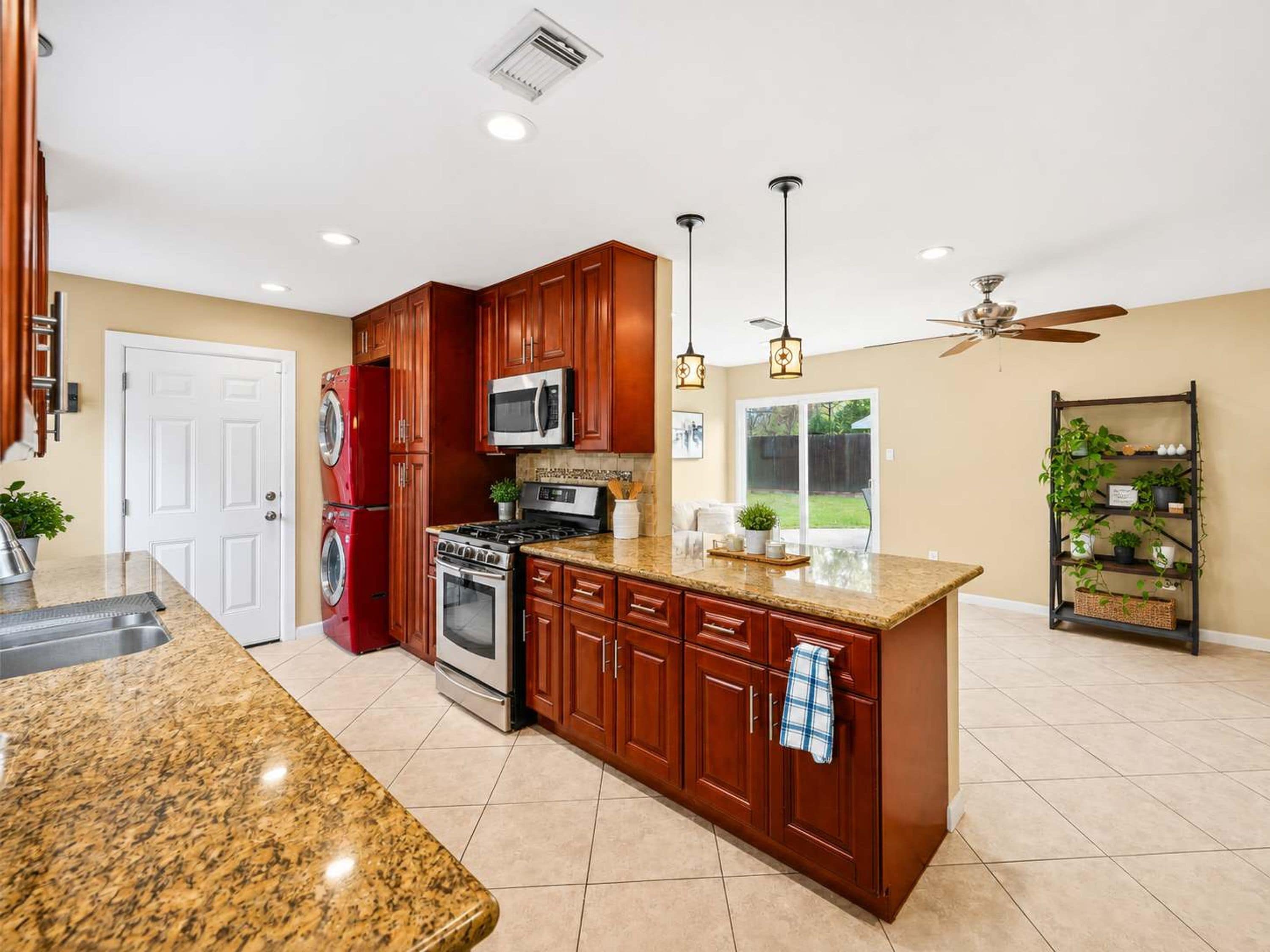 A kitchen with granite countertops, wooden cabinets, stainless steel appliances, pendant lighting, and a ceiling fan.