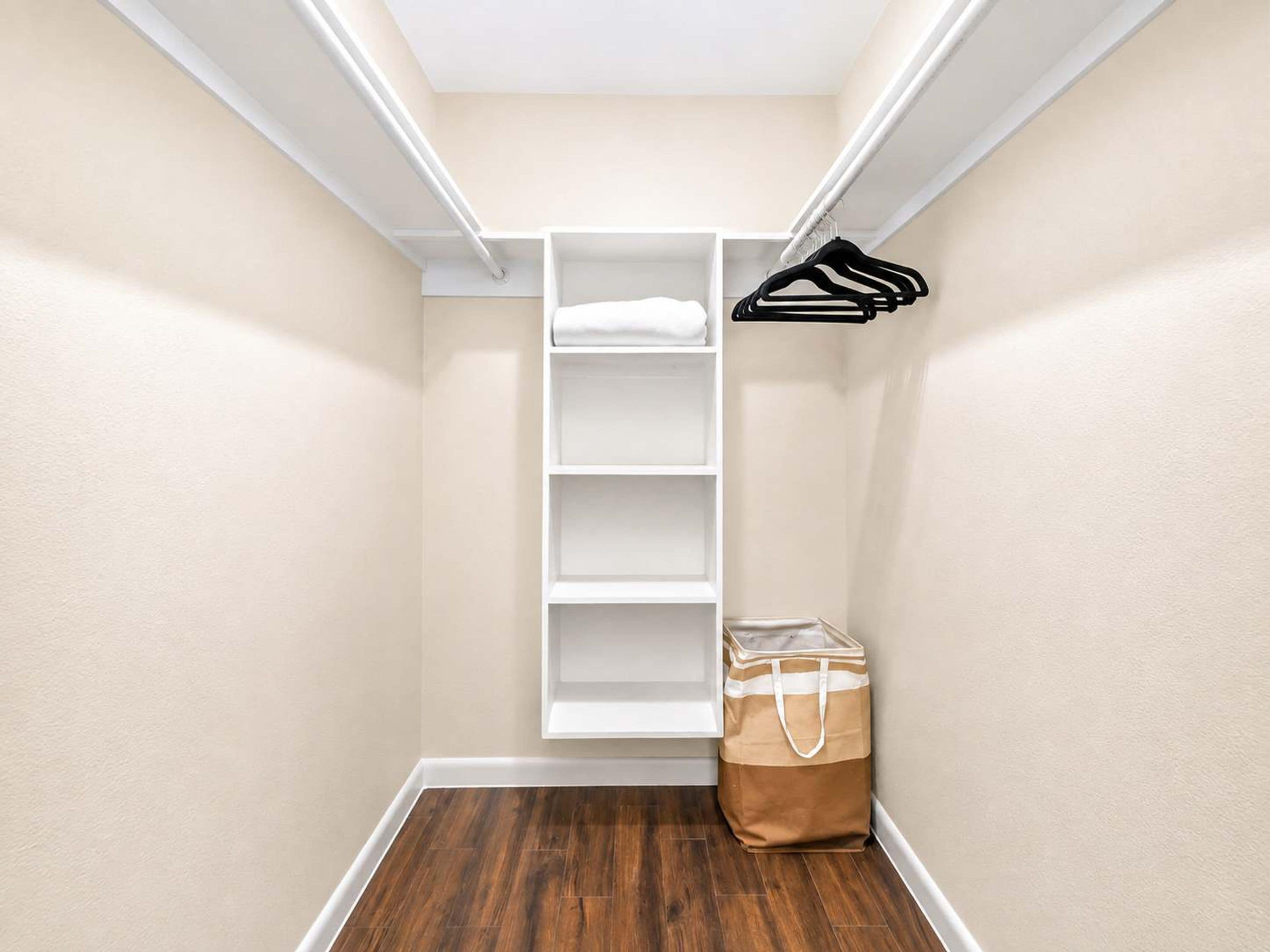 A walk-in closet with white shelving, a hanging rack, and a brown bag on the floor.