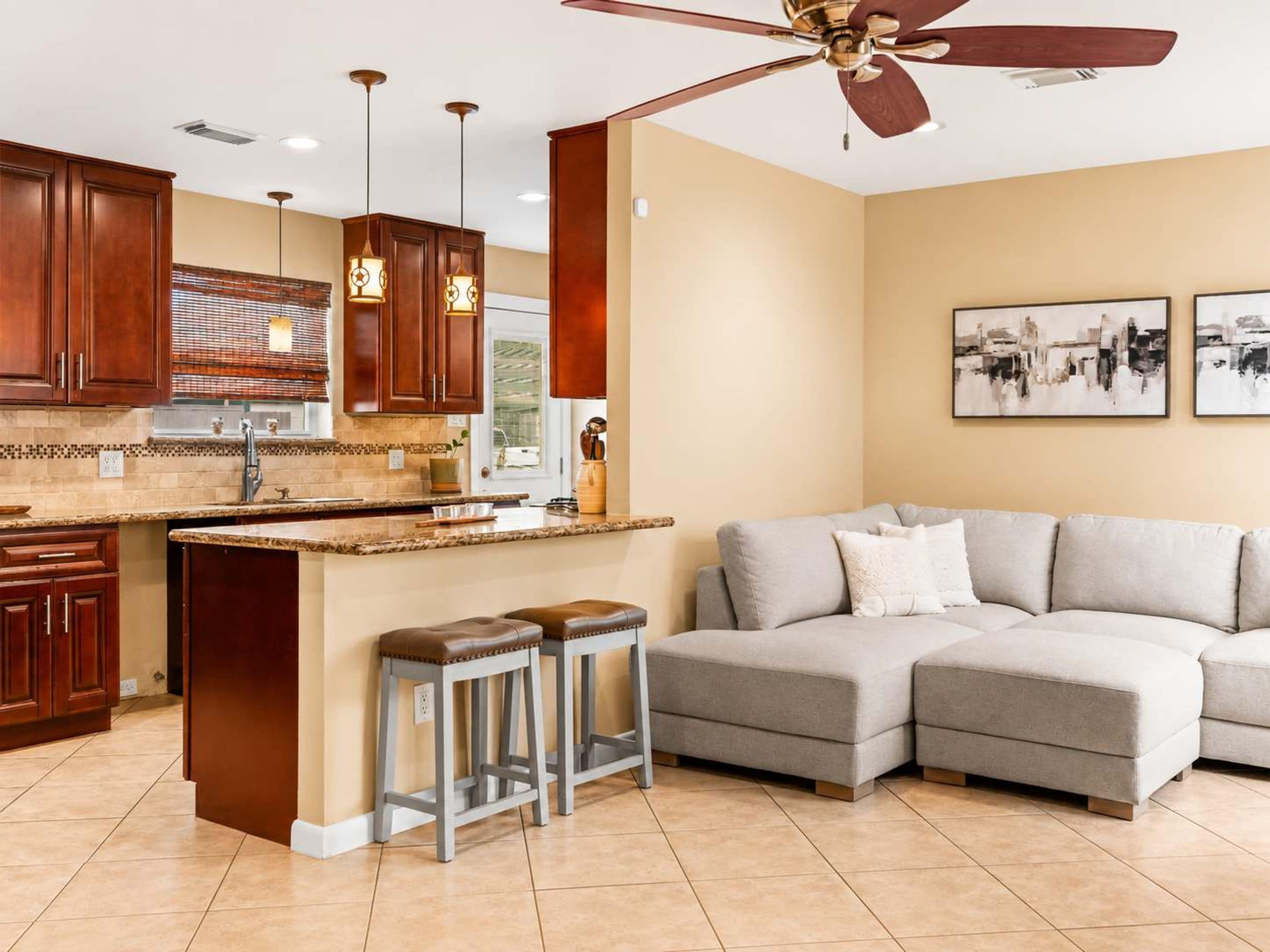 A modern kitchen with wooden cabinets, a granite countertop, and a ceiling fan.