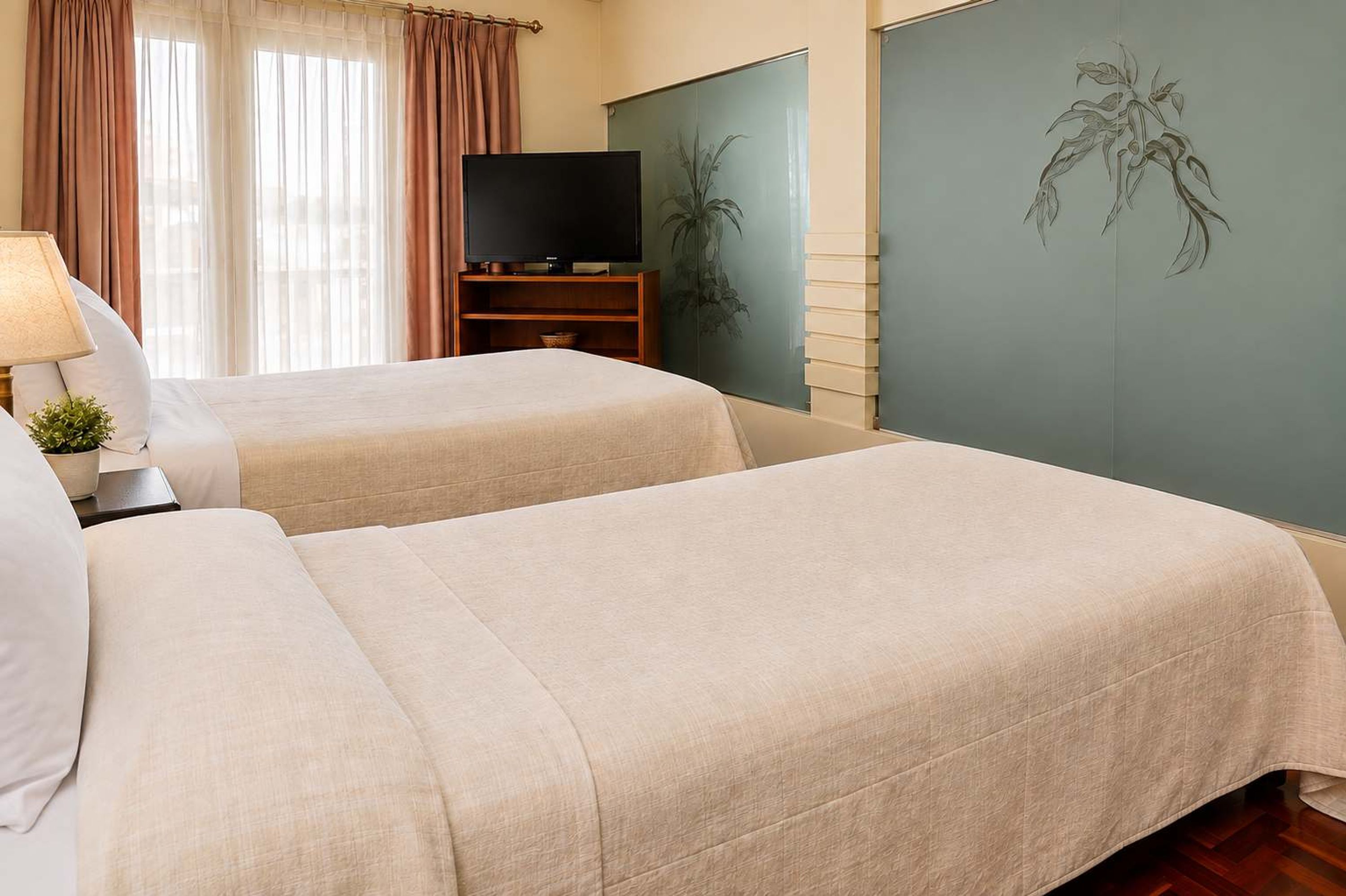 A hotel room with two beds, a television, and a wall with a plant mural.