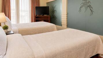 A hotel room with two beds, a television, and a wall with a plant mural.