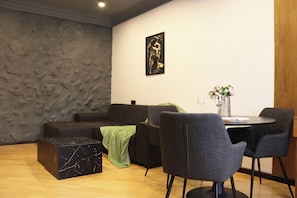 A modern living room with a stone wall, a black sofa, a green throw, a marble coffee table, and a dining area with two chairs and a vase of flowers. - Cozy 1-bedroom apartment in charming Yerevan with AC (Yerevan)
