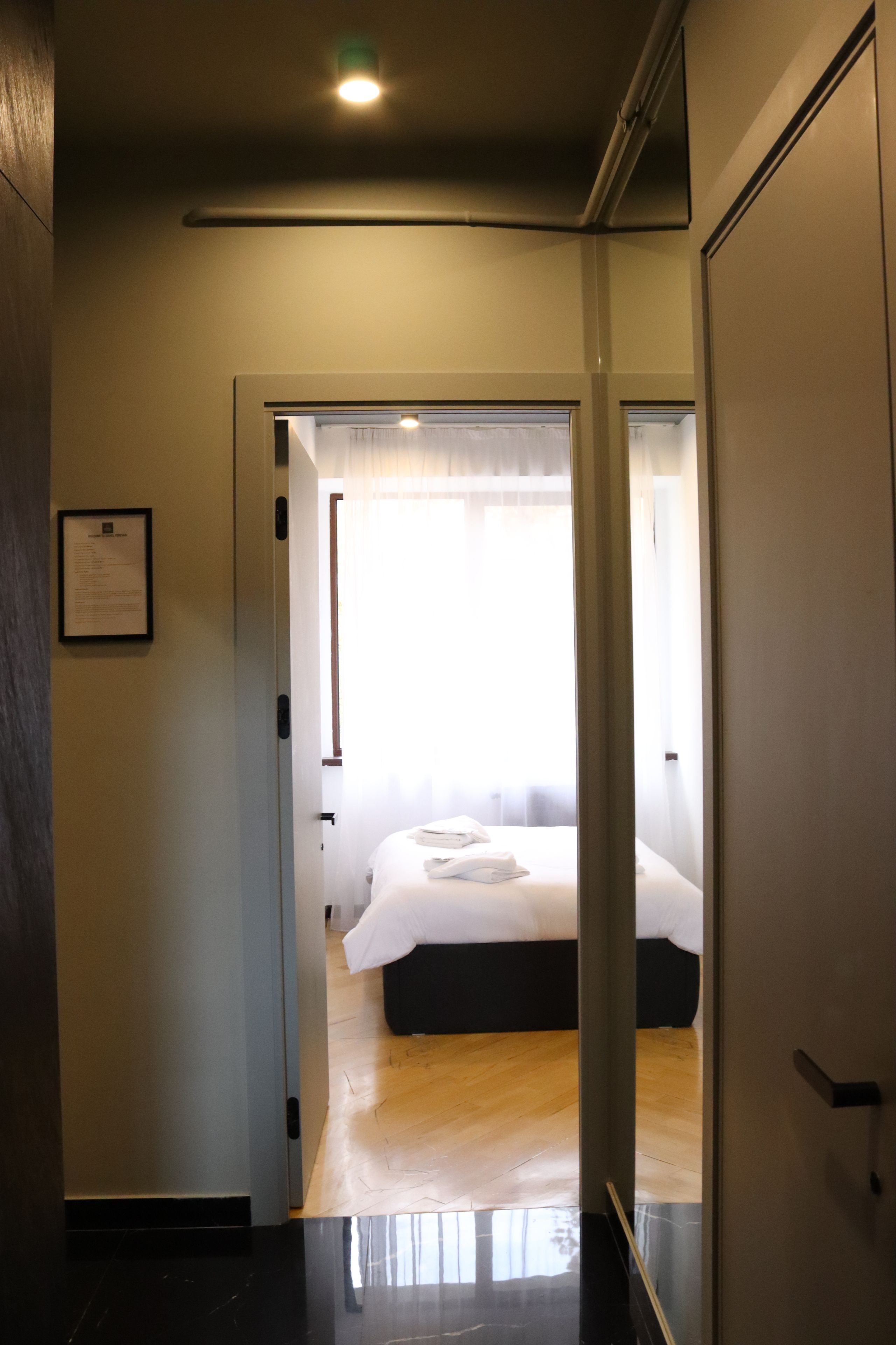 A hotel room with a bed, a door leading to another room, and a framed welcome sign on the wall.