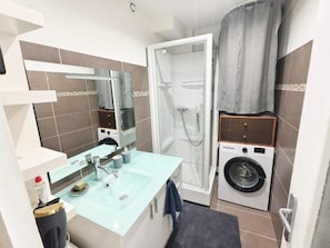 A compact bathroom with a glass sink, a shower enclosure, and a built-in washing machine. - La Bugeotte  (Marseille)