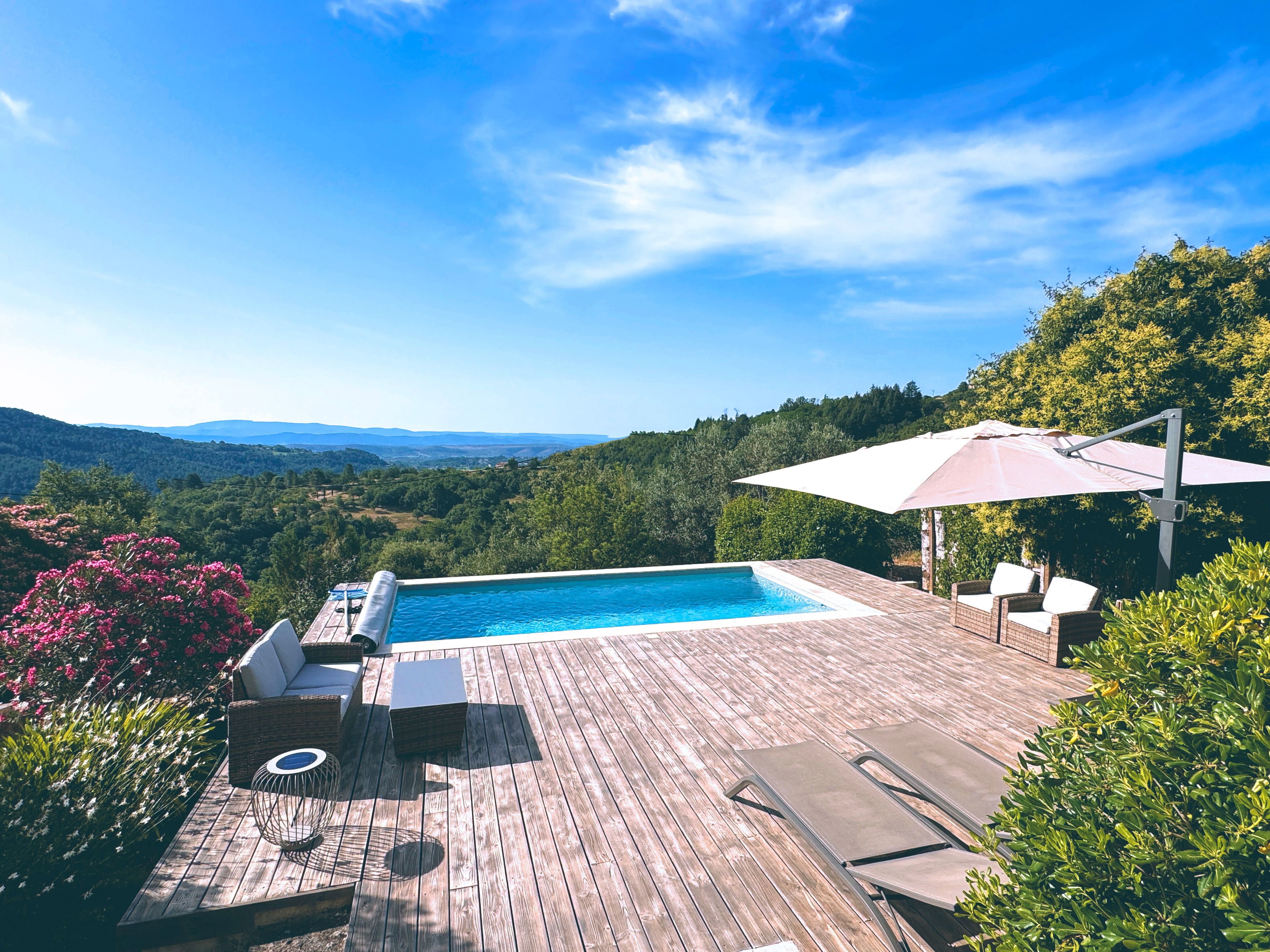 Une terrasse en bois avec une piscine, du mobilier d’extérieur et une vue sur la campagne.