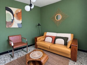 A room with a green wall, a yellow sofa, a red chair, a round coffee table, and a modern mirror. - Villa 'La Rouvière' with pool, panoramic view, Wi-Fi and air conditioning (Chassiers)