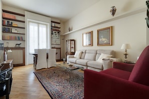 A living room with a sofa, armchair, coffee table, and bookshelf. - A spacious and charming 105 square-meter apartment, with vintage and classic-style décor, ideal for five people, located on the first floor (elevator available, though NOT suitable for people with disabilities) of a building near the lively, modern, and (Milan)