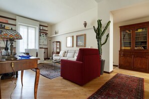 Una sala de estar con un sillón rojo, un sofá blanco, una mesa de centro de madera y una estantería.