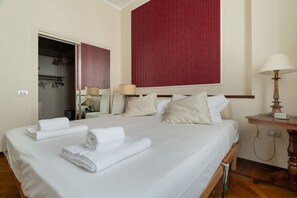 A hotel room with a large bed, a wardrobe, a mirror, and a red accent wall. - A spacious and charming 105 square-meter apartment, with vintage and classic-style décor, ideal for five people, located on the first floor (elevator available, though NOT suitable for people with disabilities) of a building near the lively, modern, and (Milan)