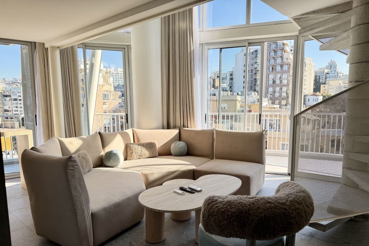 A modern living room with a sectional sofa, a round coffee table, and a view of the city through large windows.