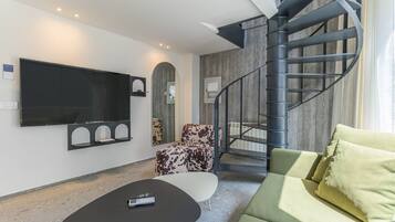 A modern living room with a flat-screen TV, a sofa, a coffee table, and a spiral staircase.