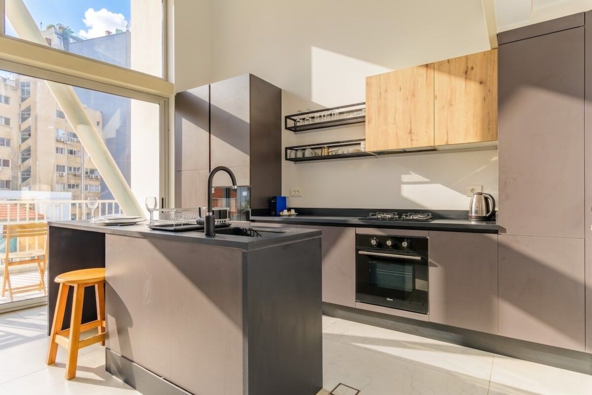 A modern kitchen with a central island, built-in appliances, and a large window providing natural light.