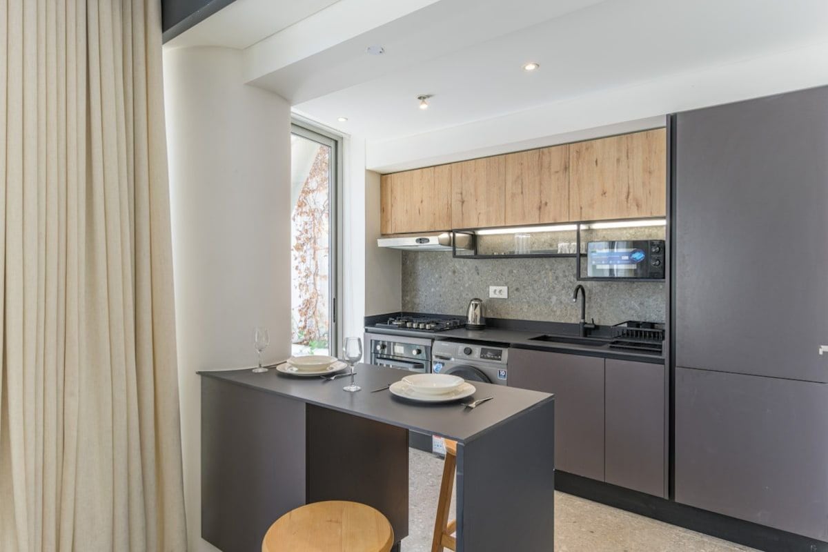 A modern kitchen with a central island, built-in appliances, and a large window.