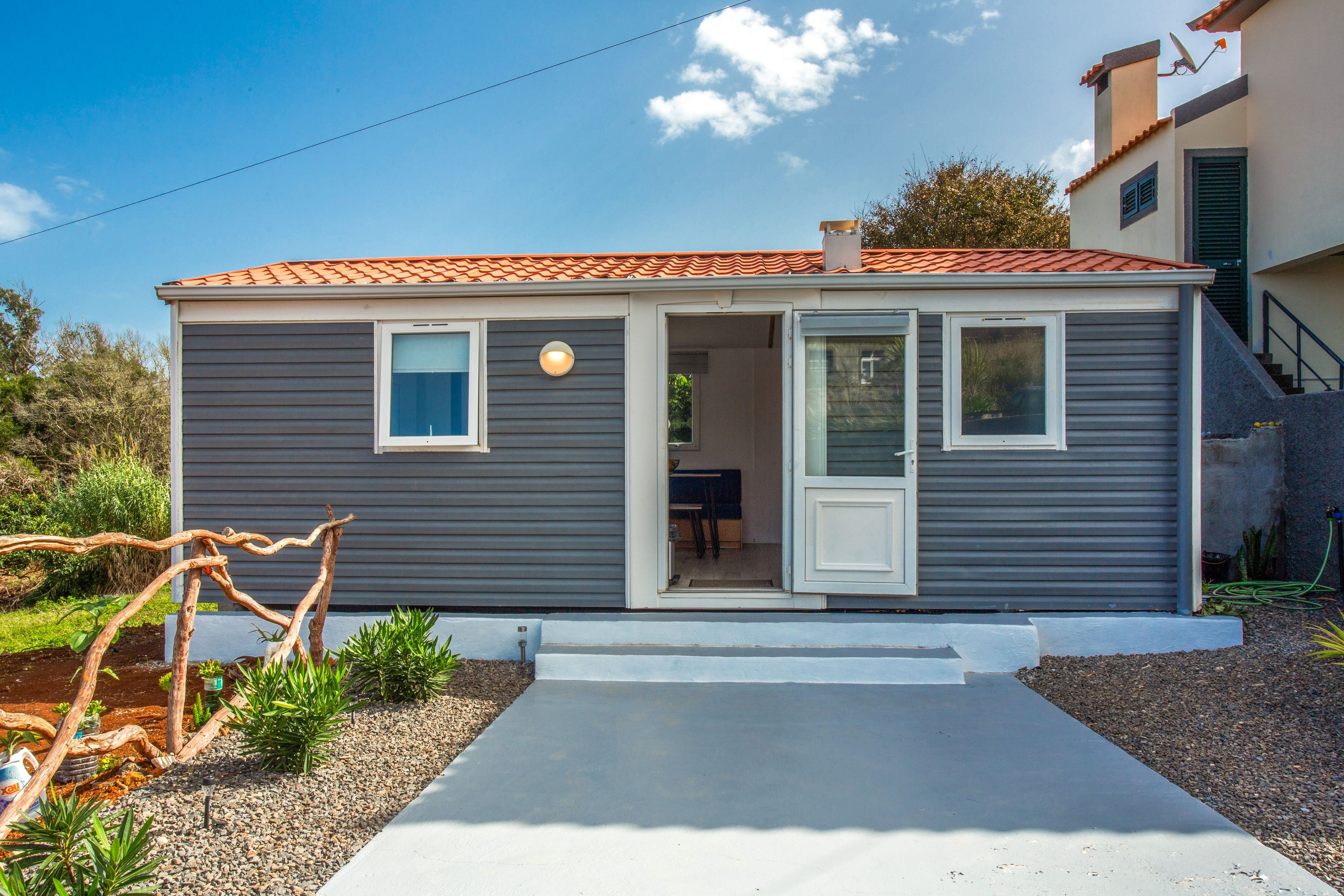 Une maison de plain-pied, avec une façade grise, un toit recouvert de tuiles rouges et une porte d’entrée.