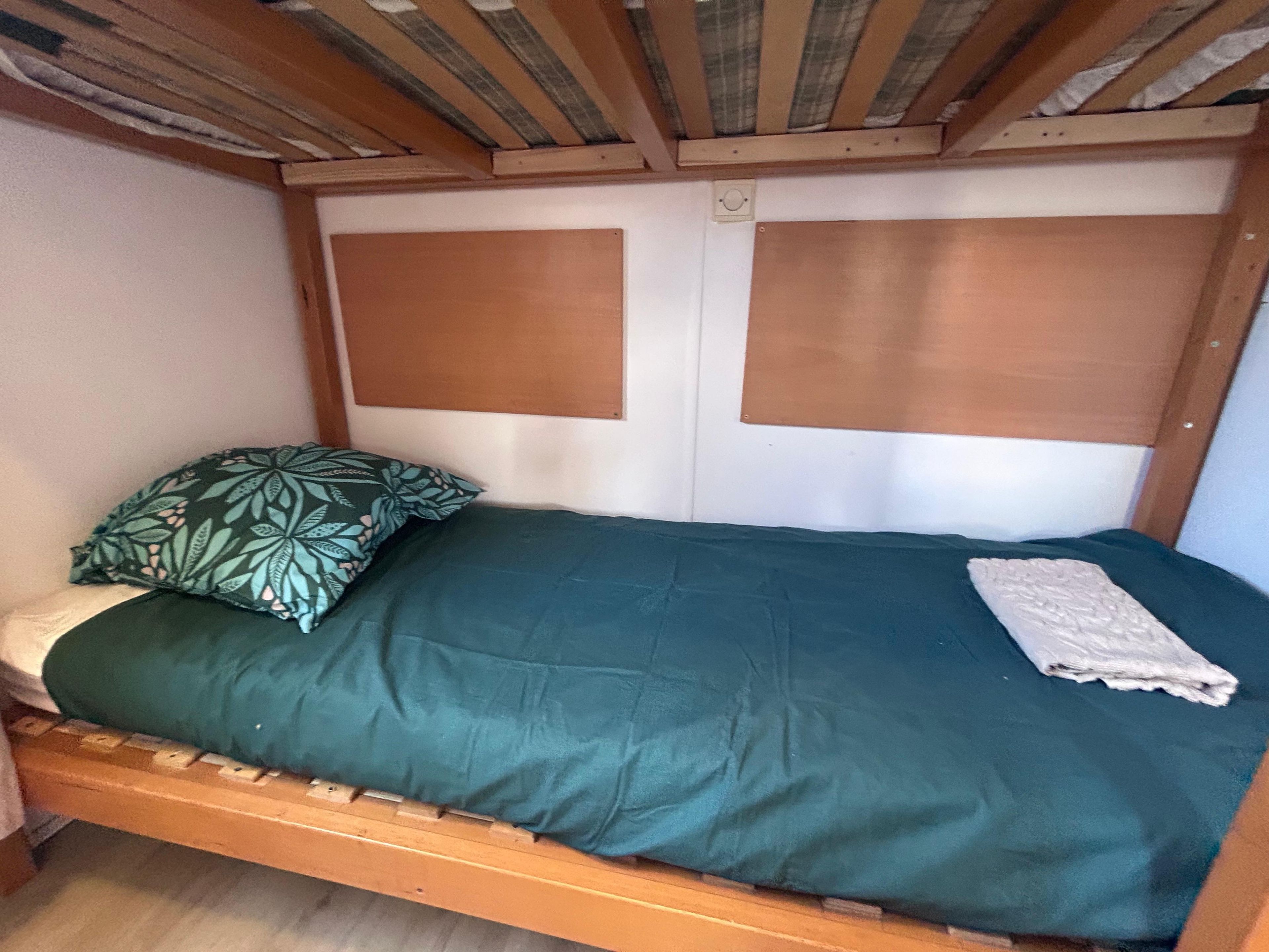 Una cama individual con colcha verde y almohada estampada, cabecero de madera y manta blanca.